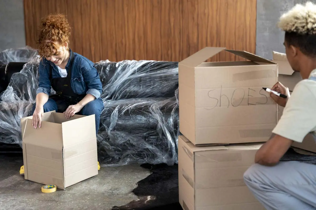 Couple packing and labeling cardboard boxes for moving day.