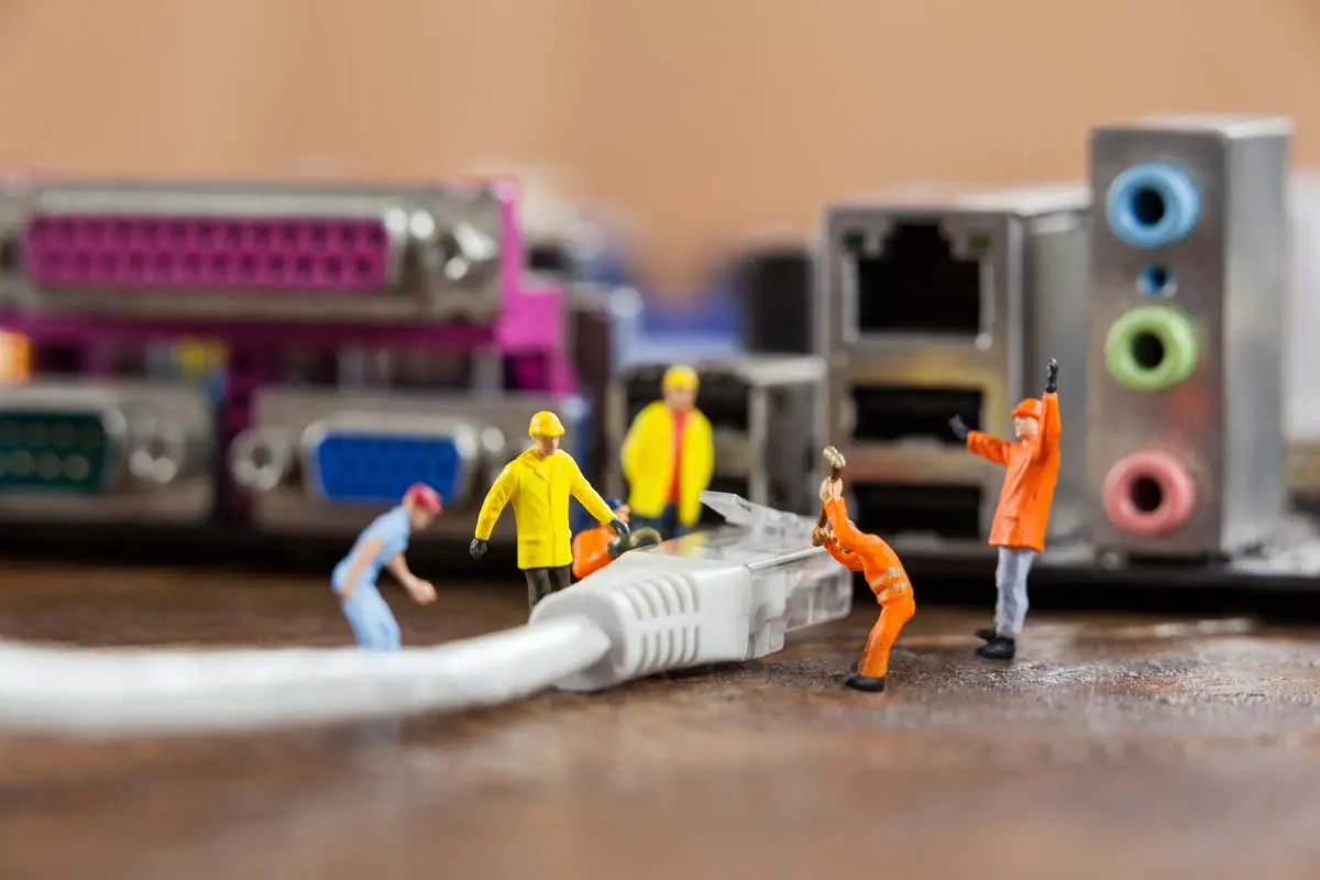Miniature workers repairing or inspecting a network cable near computer ports.