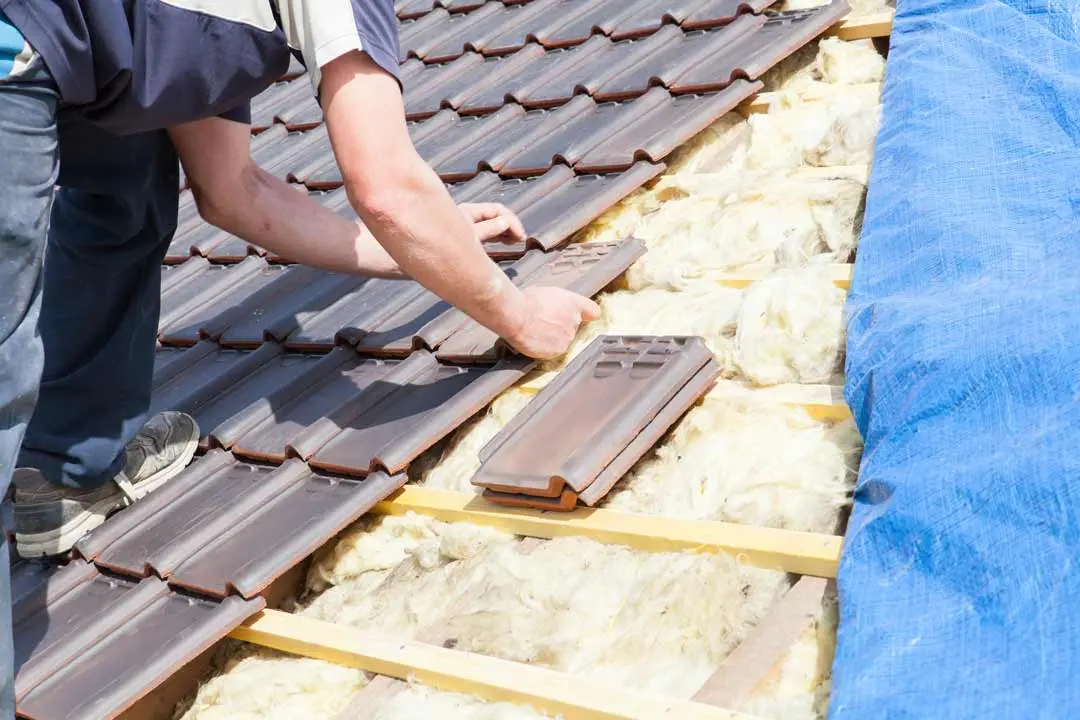 Worker installing roof tiles over insulation with a blue tarp on the side.