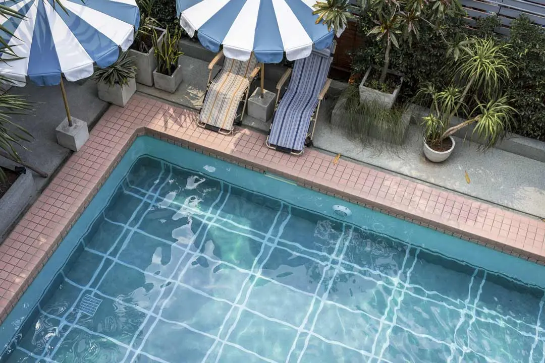 Outdoor pool with striped lounge chairs, blue umbrellas, and potted plants along the deck.