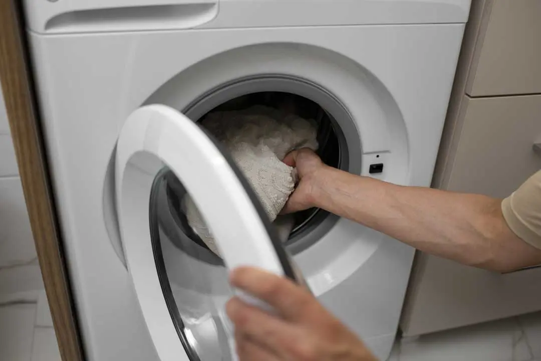 Hand placing clothes into a front-loading washing machine at home.
