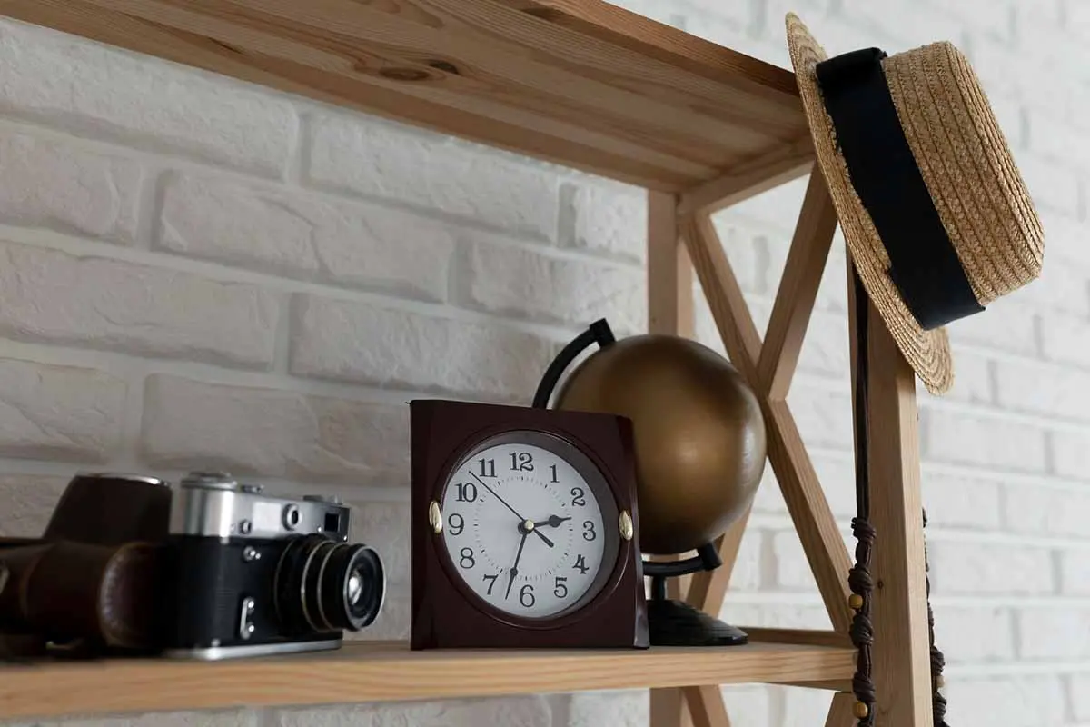Wooden shelf holding a vintage camera, clock, globe, and a straw hat, adding character to the space with nostalgic decor.