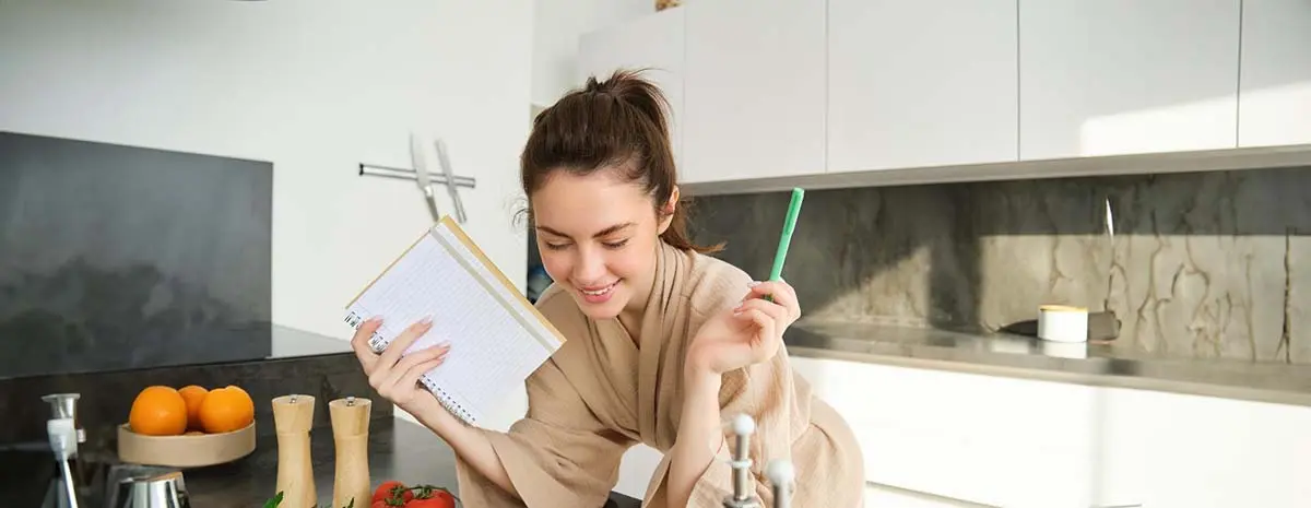 Smiling woman holding a notepad in a clean kitchen.