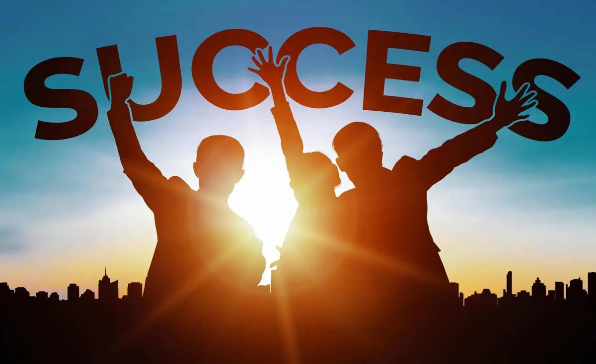 Silhouette of three people celebrating under the word success against a sunset background.