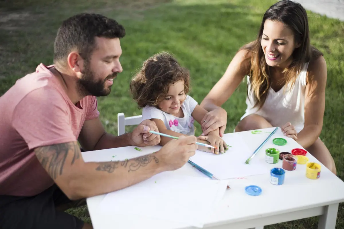 Parents painting with their daughter outdoors, enjoying family time.