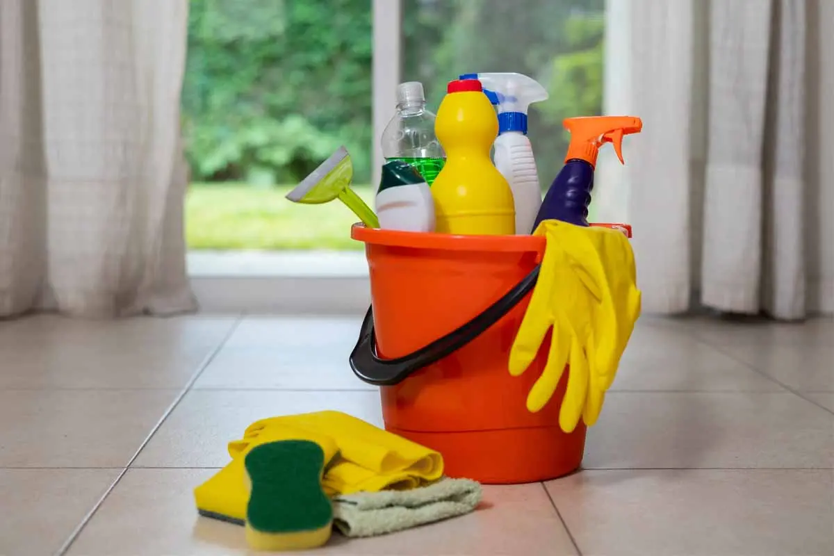 Orange bucket filled with cleaning products, gloves, and sponges, ready for household cleaning tasks.