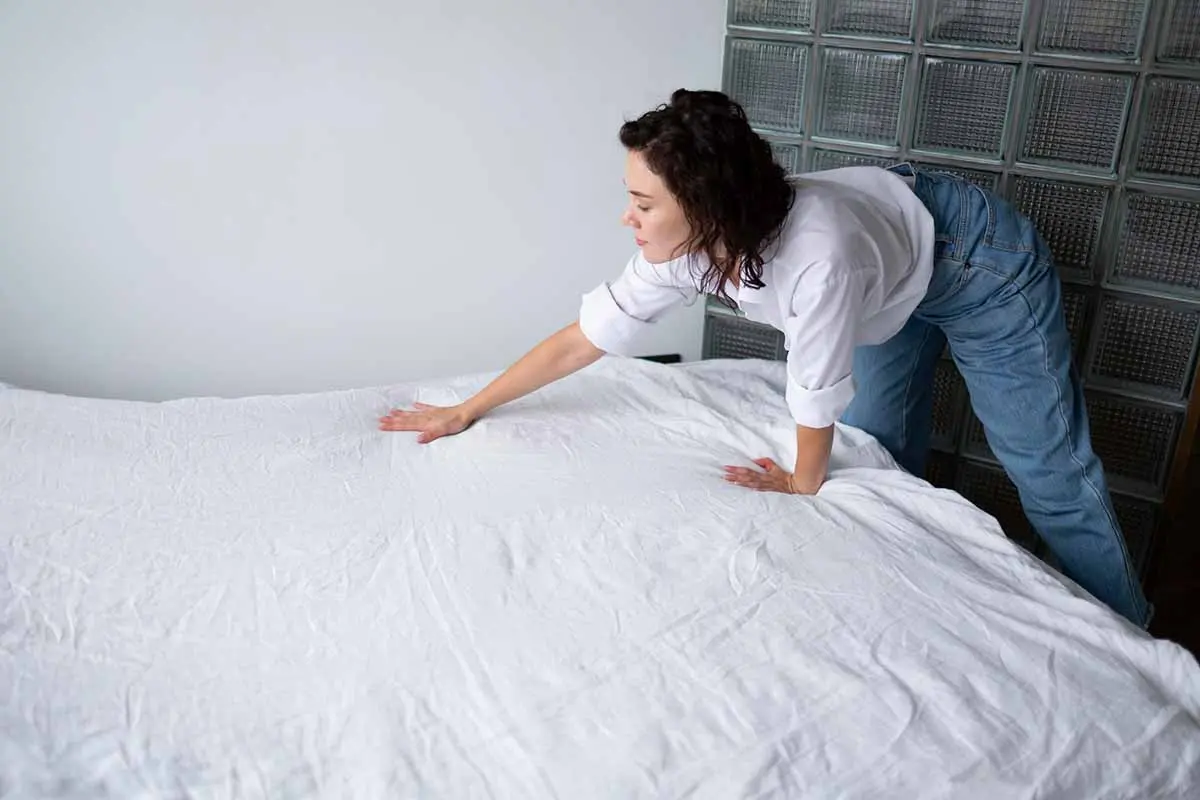 Woman smoothing out a white bedsheet on a neatly made bed, promoting a clutter-free, organized space.