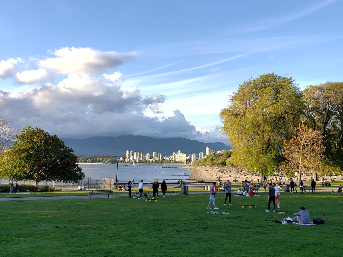 Kitsilano Beach park with people playing and city skyline views.