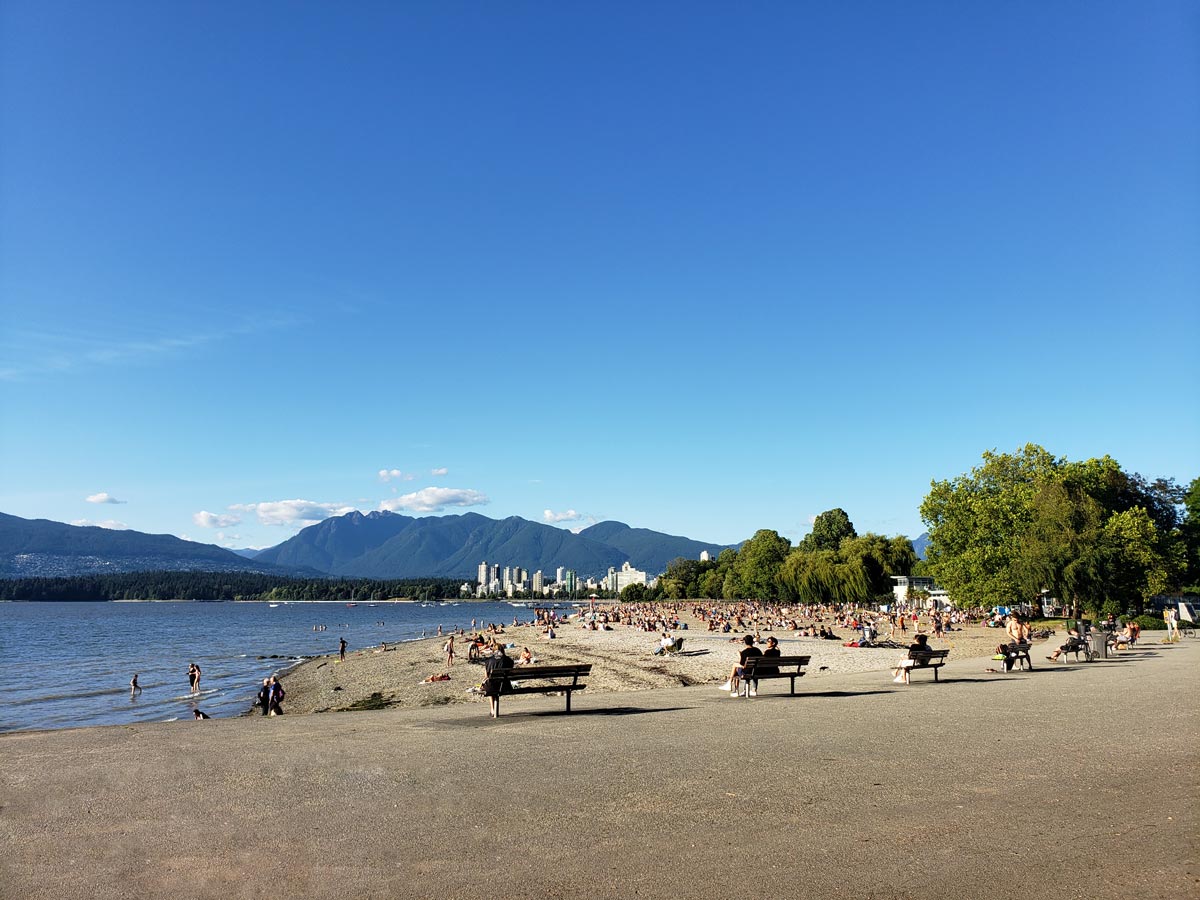 Kitsilano Beach with people enjoying the shore and mountain views.