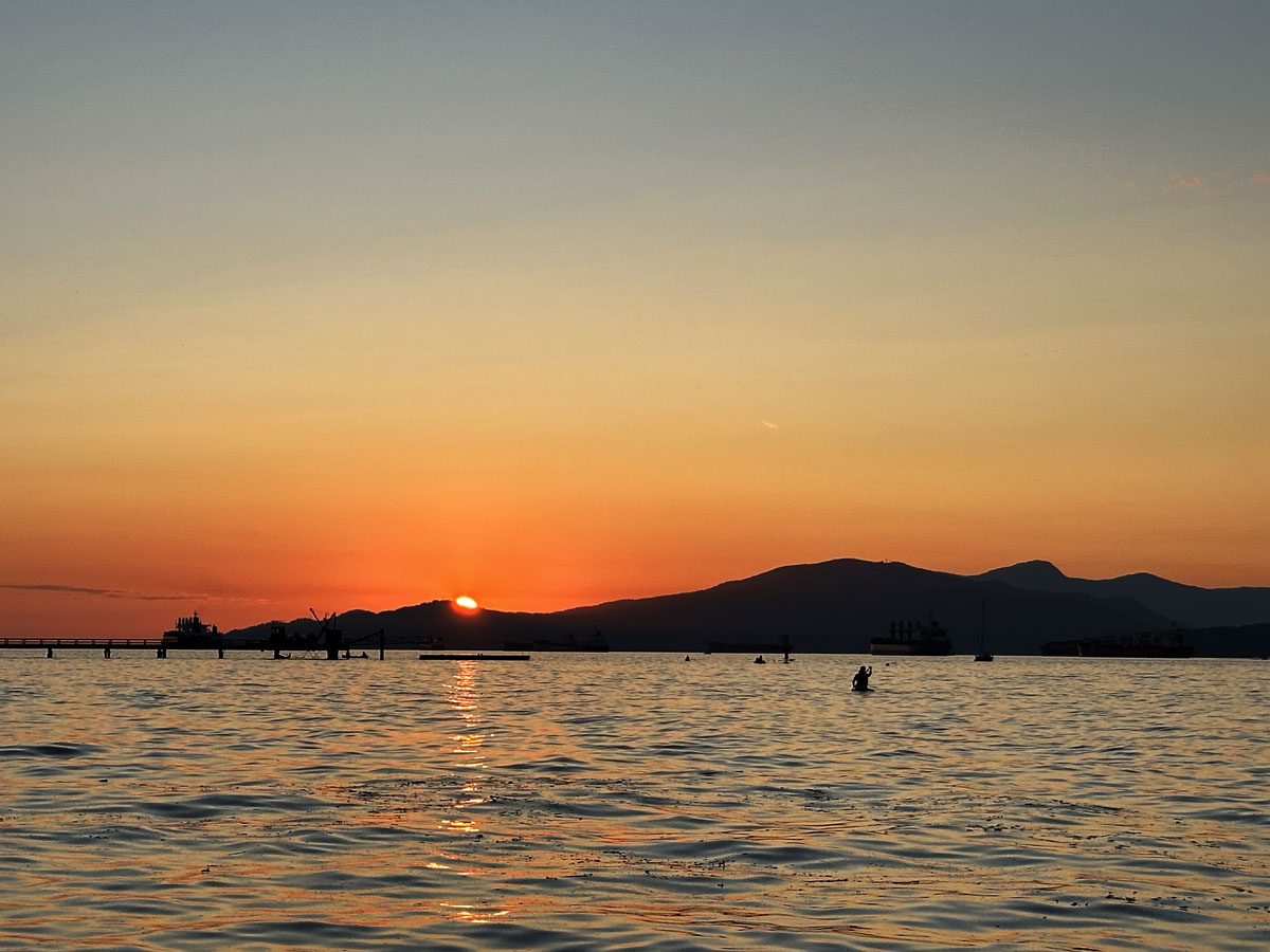 Sunset over the ocean at Kitsilano Beach with silhouetted paddlers.