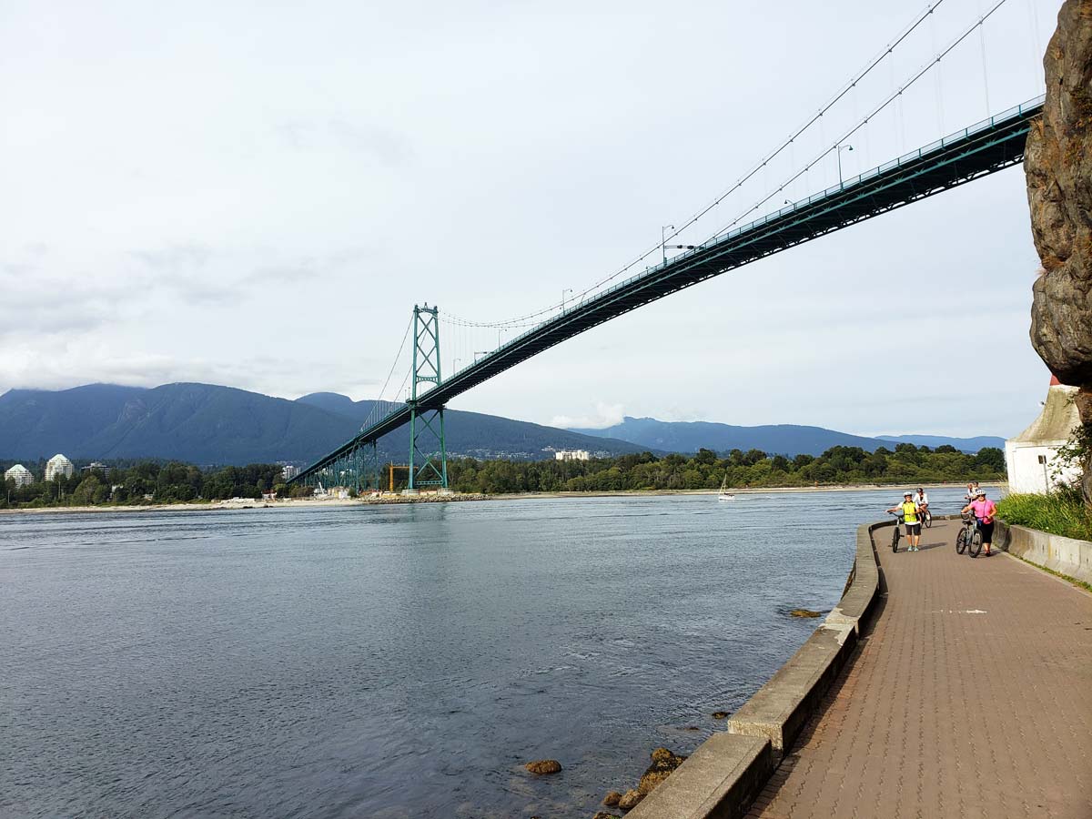Lions Gate Bridge view from Stanley Park Seawall with cyclists.