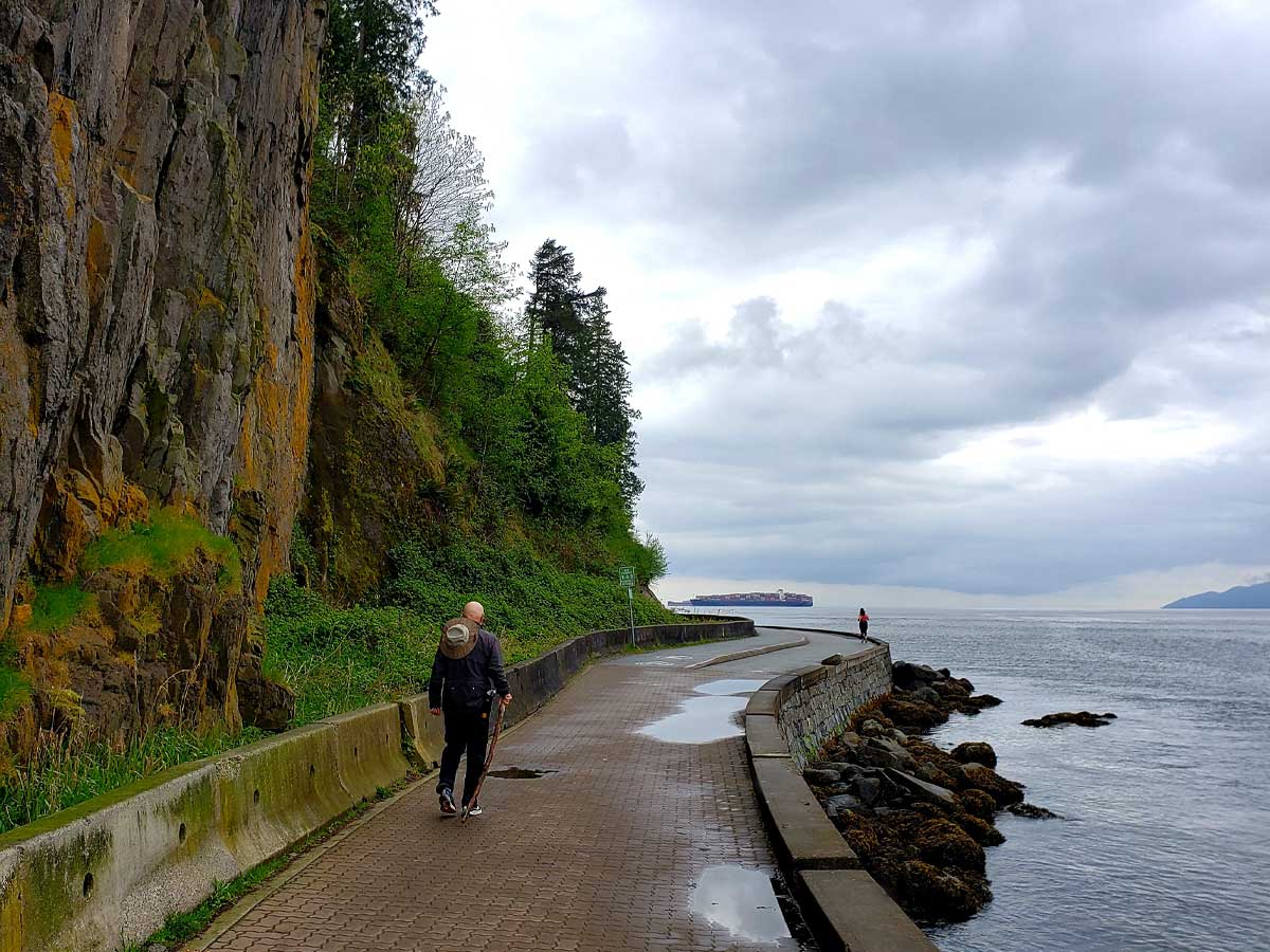 A person walking along the Stanley Park Seawall on a cloudy day.