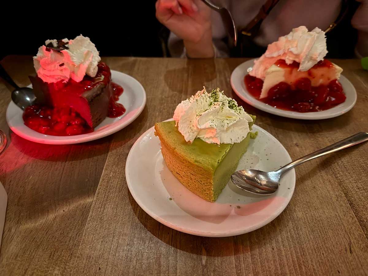 Three slices of cheesecake with whipped cream and berry sauce.