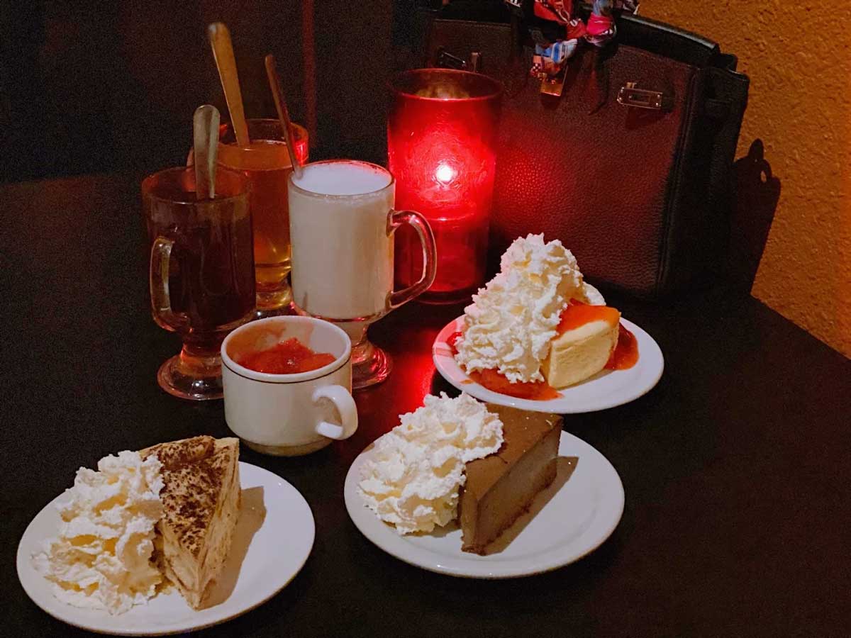 Dessert table with cheesecake slices, whipped cream, and hot drinks.