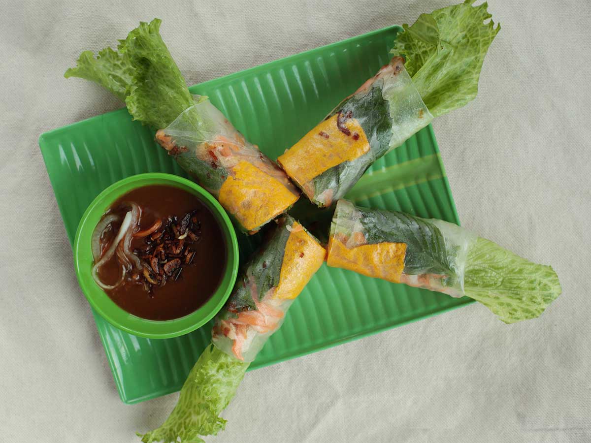 Fresh Vietnamese spring rolls with dipping sauce on a green plate.