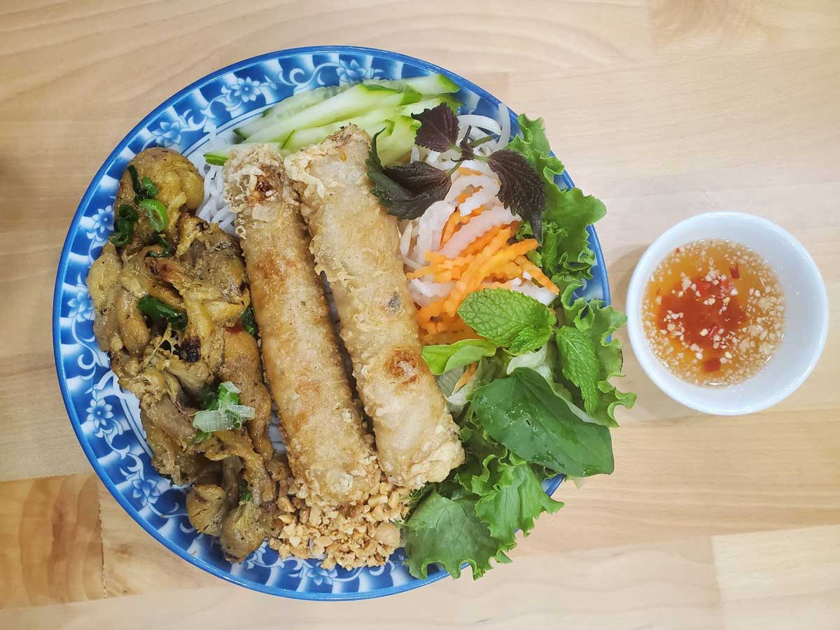 Vermicelli bowl with grilled chicken, spring rolls, and herbs.