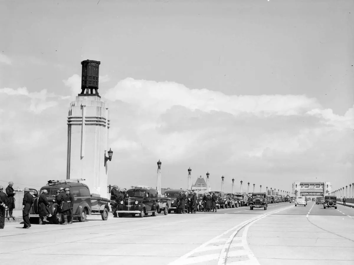 Historic view of Burrard Bridge with original brazier towers and vintage cars lined up.
