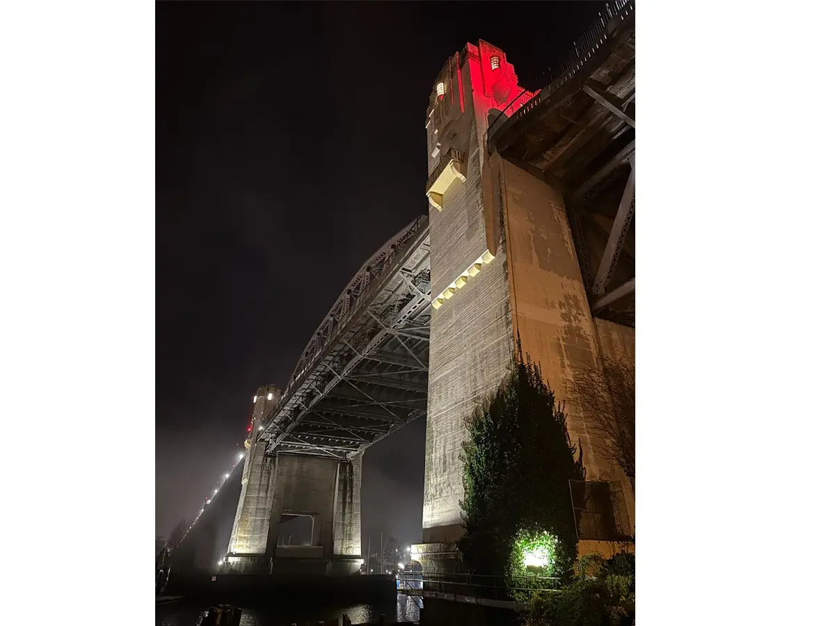 Burrard Bridge illuminated at night with red lights on tower.