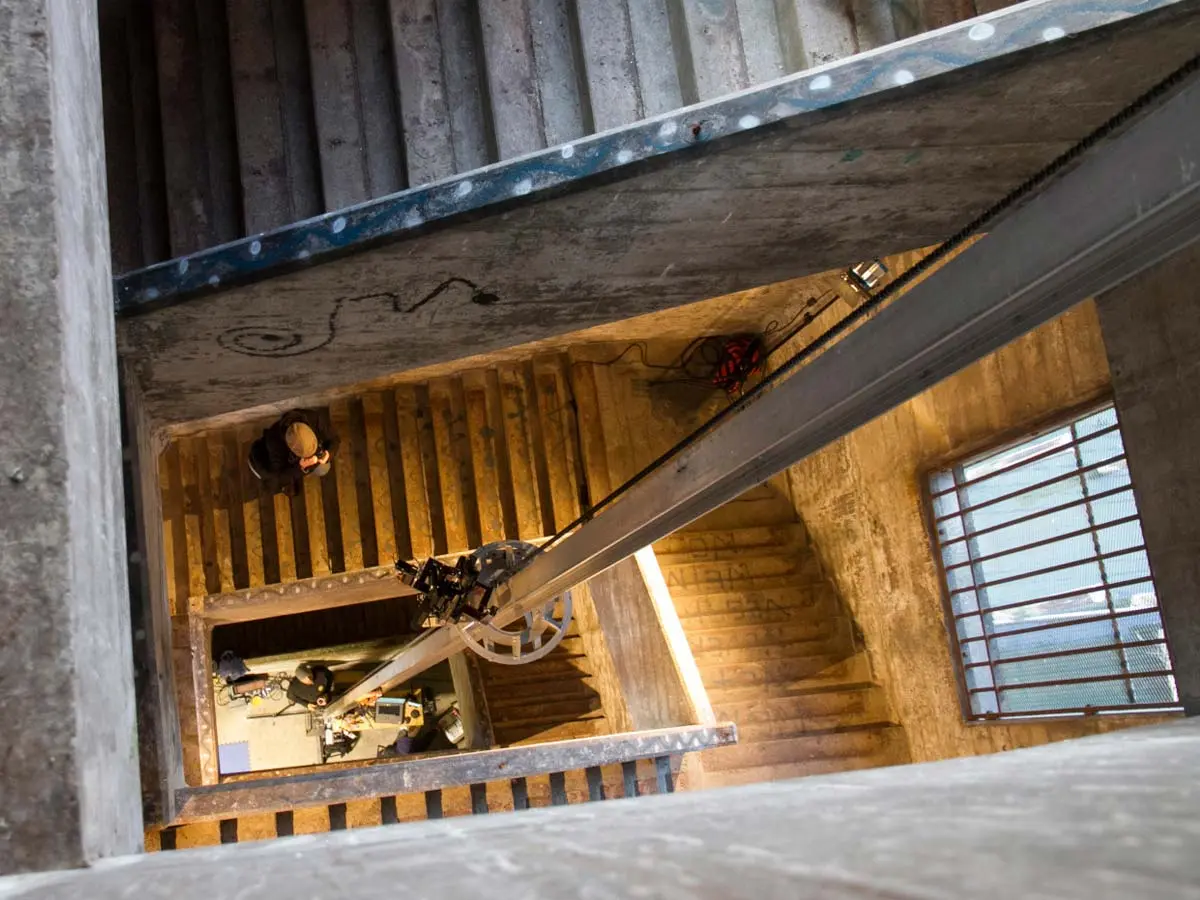 View inside the hidden stairwell of Burrard Bridge, showing concrete steps, graffiti, a camera rig setup, and a barred window.
