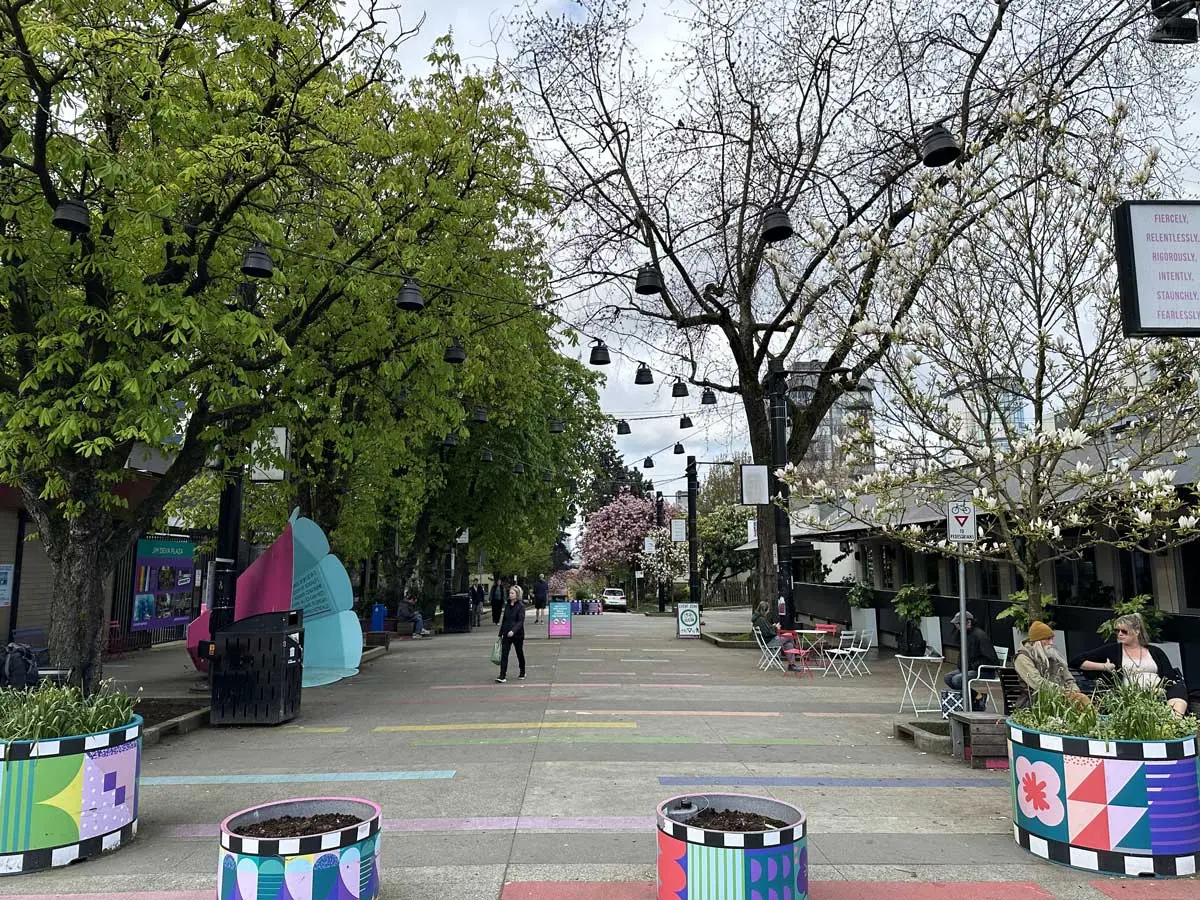 Colorful pedestrian zone at Bute and Davie Street with trees, seating, and public art installations.