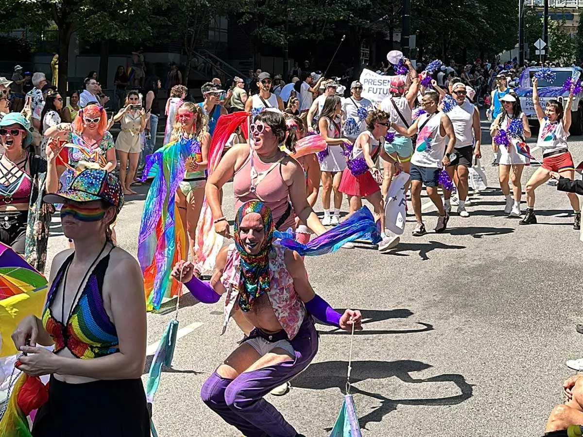 People dancing and celebrating in colorful outfits at Vancouver Pride Parade on Davie Street.