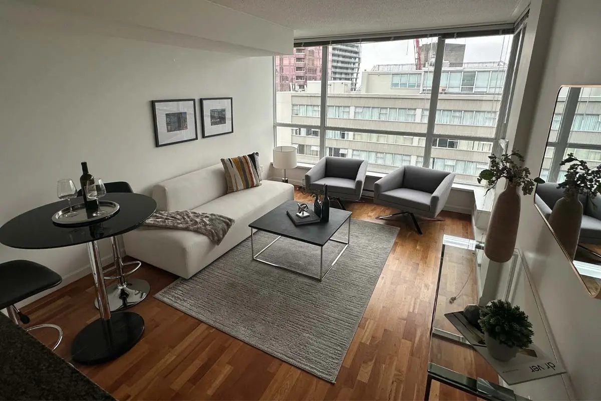 Modern furnished apartment with large windows, a white sofa, and city views in downtown Vancouver.