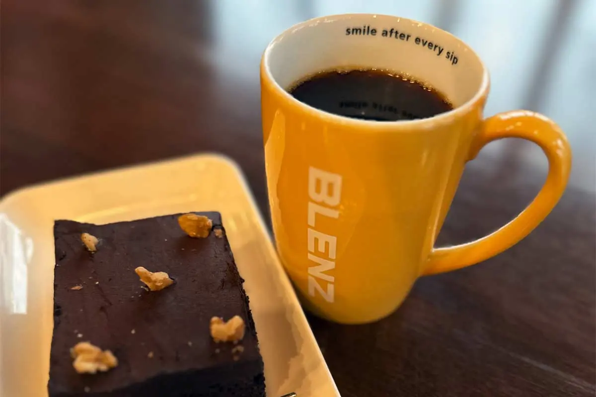 Yellow Blenz coffee mug with black coffee and a chocolate brownie topped with walnuts on a white plate.