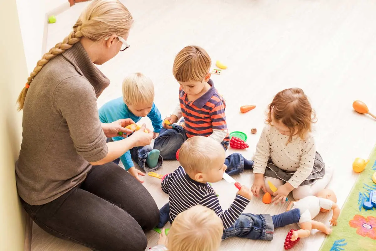 Teacher sitting on the floor with young children playing with toy food at a daycare.