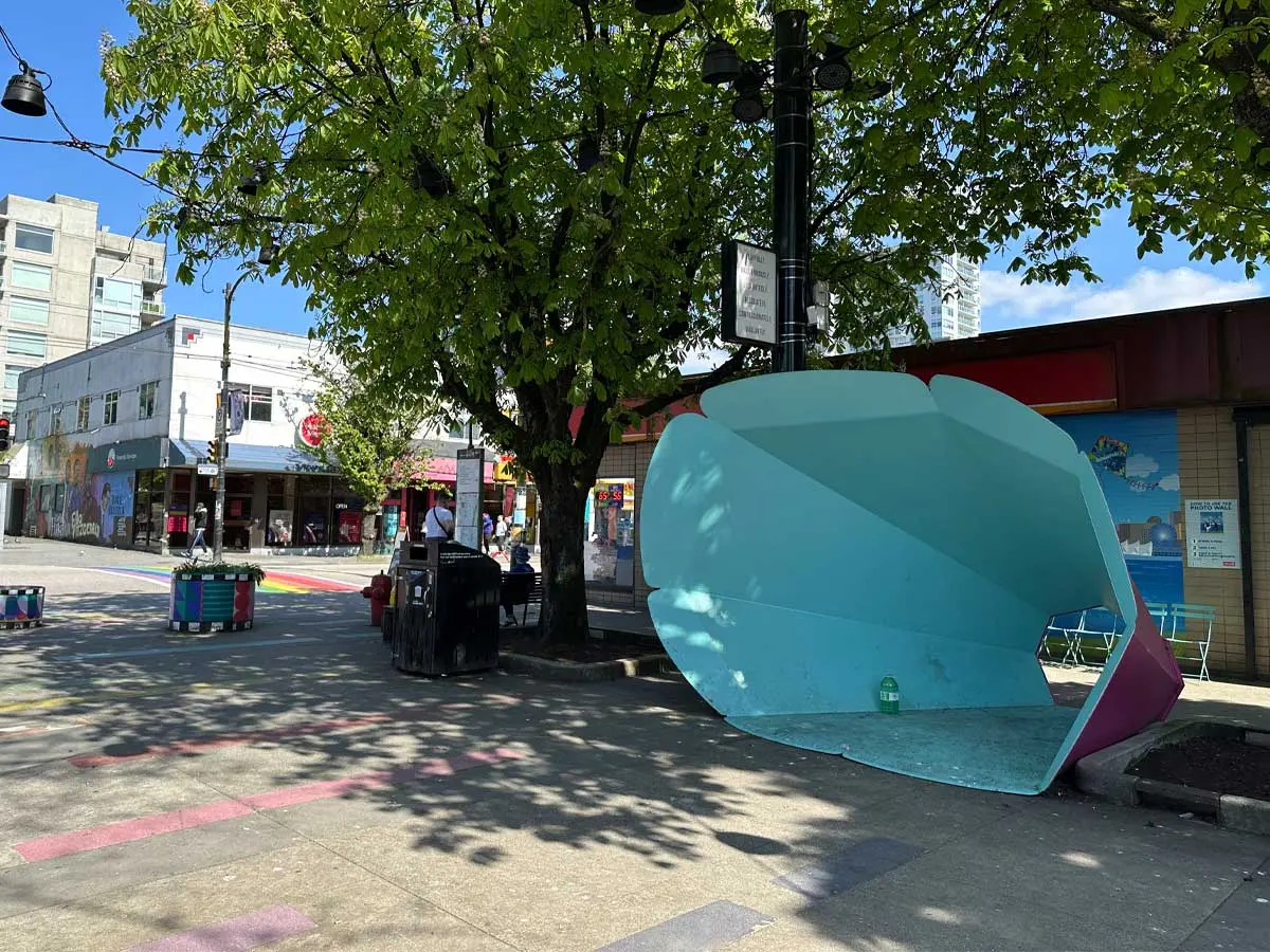 Colorful megaphone sculpture at Jim Deva Plaza with rainbow crosswalk and shops in the background.