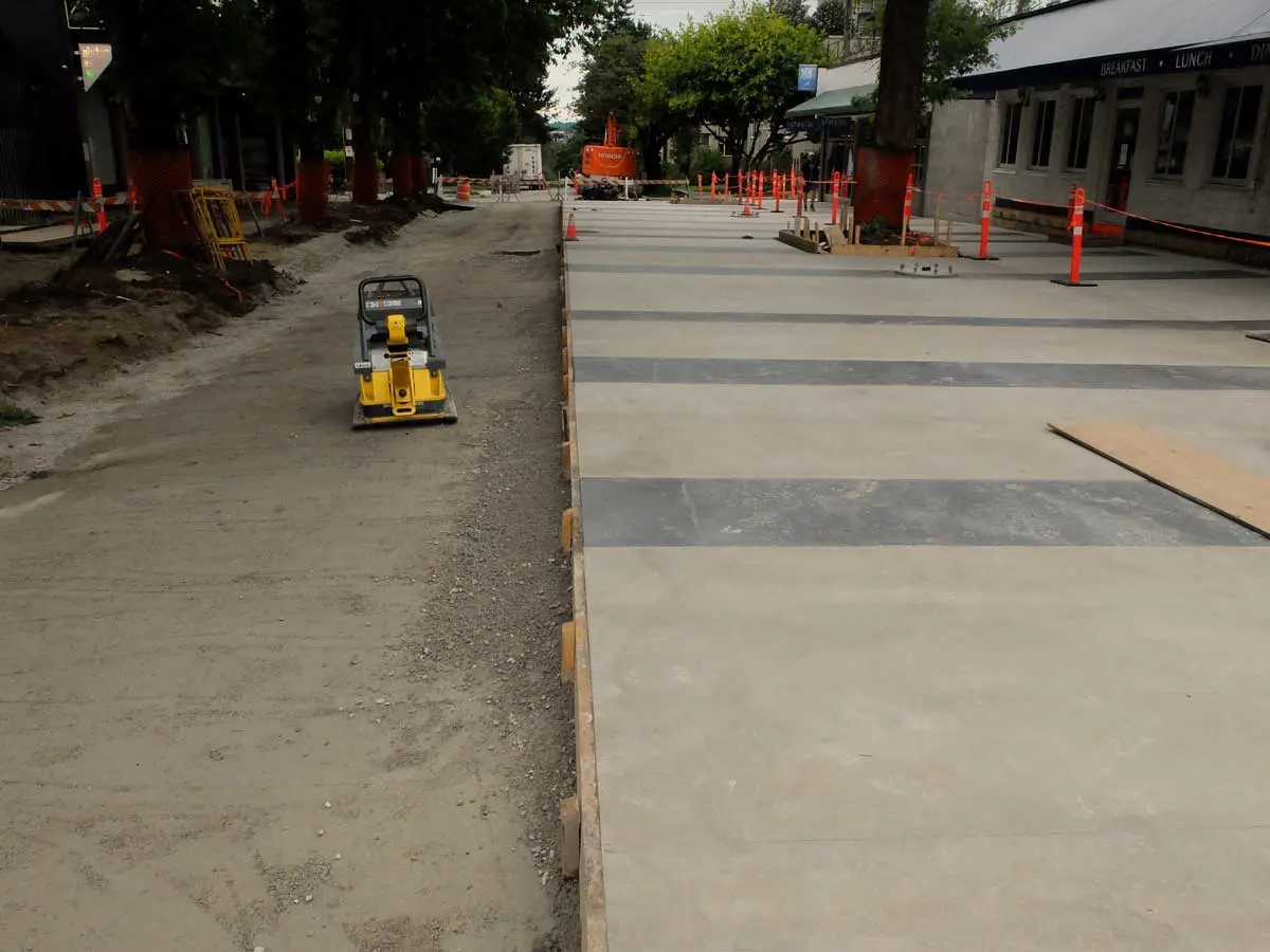 Jim Deva Plaza under construction with new concrete pavement and a small yellow compactor on site.