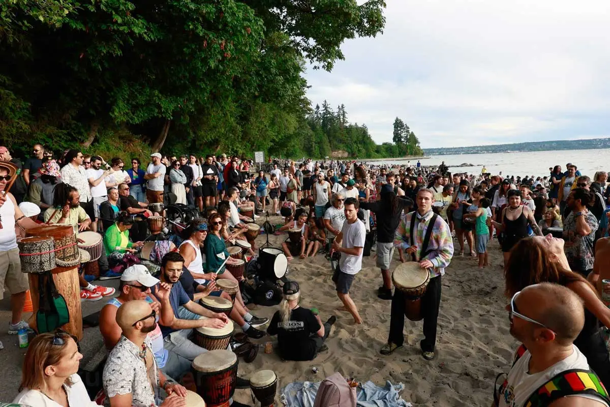 Crowd drumming, dancing, and gathering at Third Beach in Vancouver.