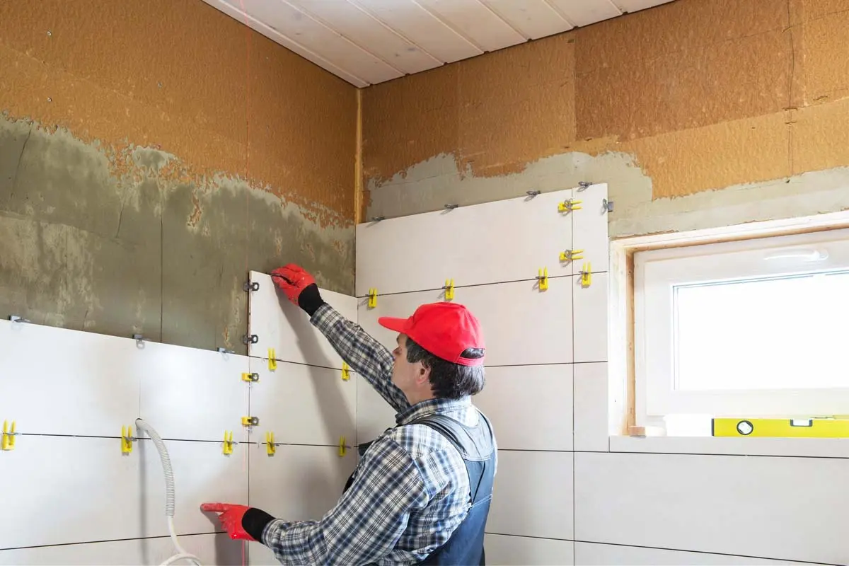 Worker installing large white tiles on a bathroom wall during renovation.