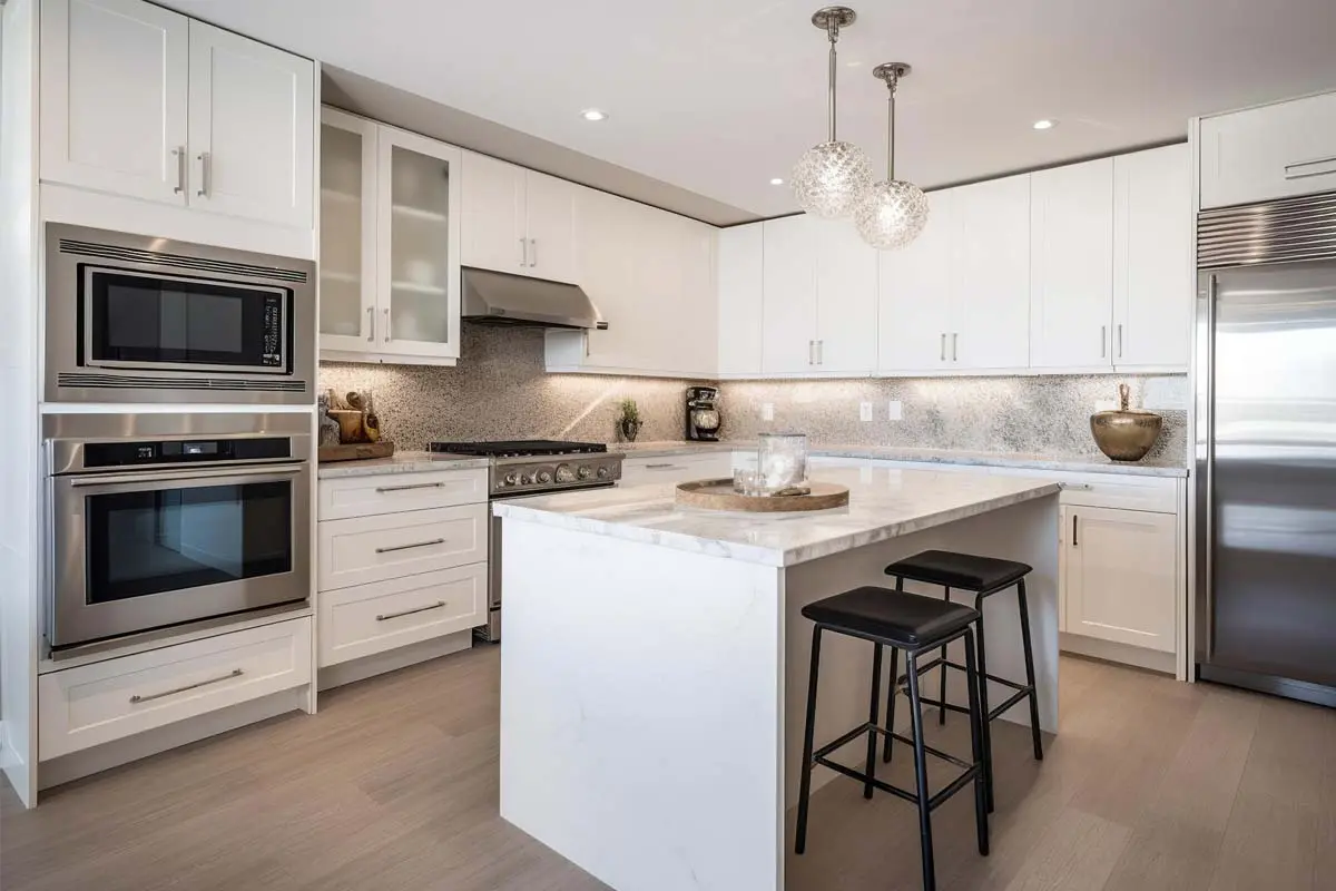 Sleek kitchen with white cabinetry, stainless steel appliances, marble island, and pendant lights above the island.