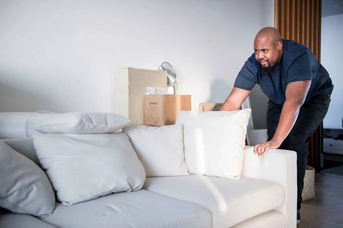 Man adjusting a white sofa in a living room.