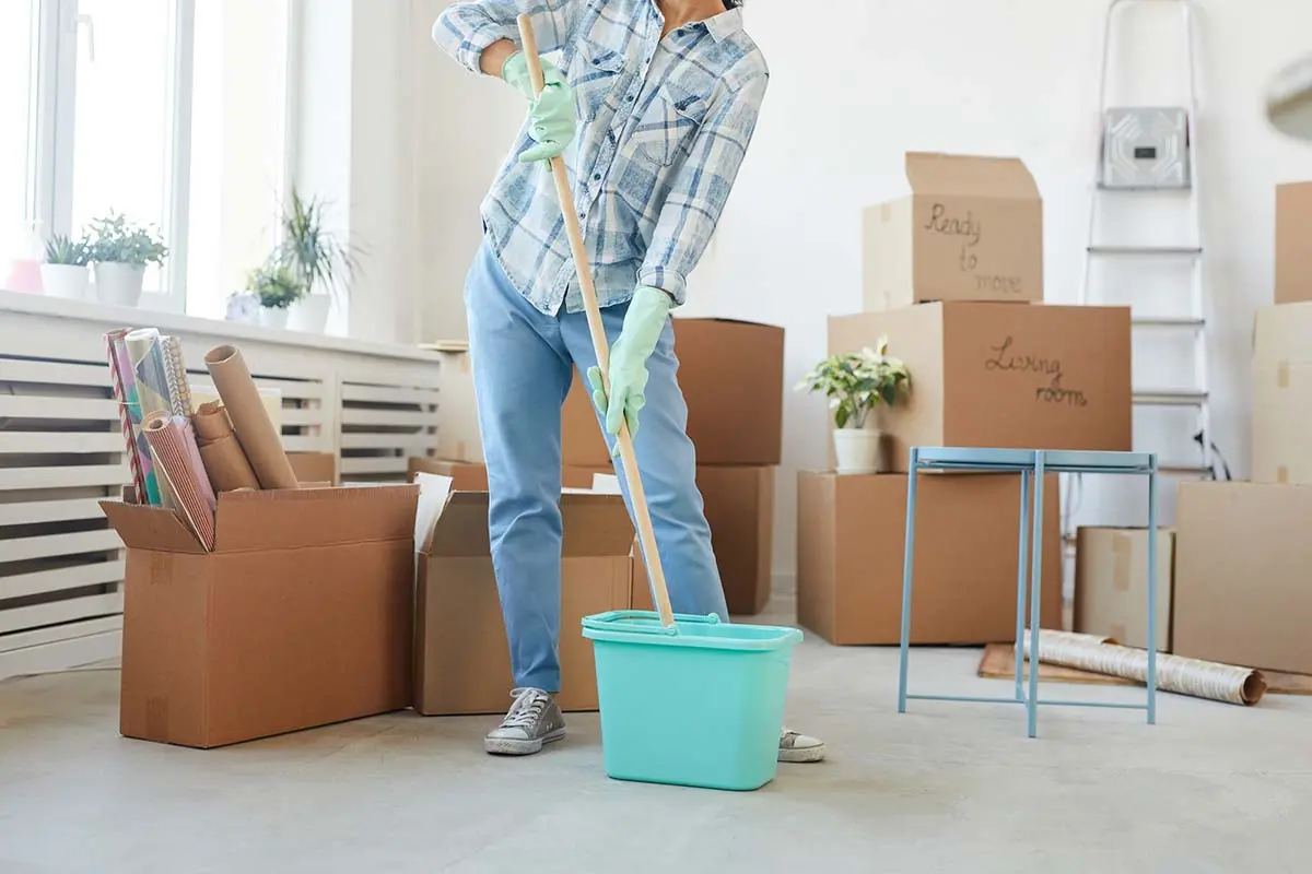 Person mopping a floor in a room with moving boxes and plants.