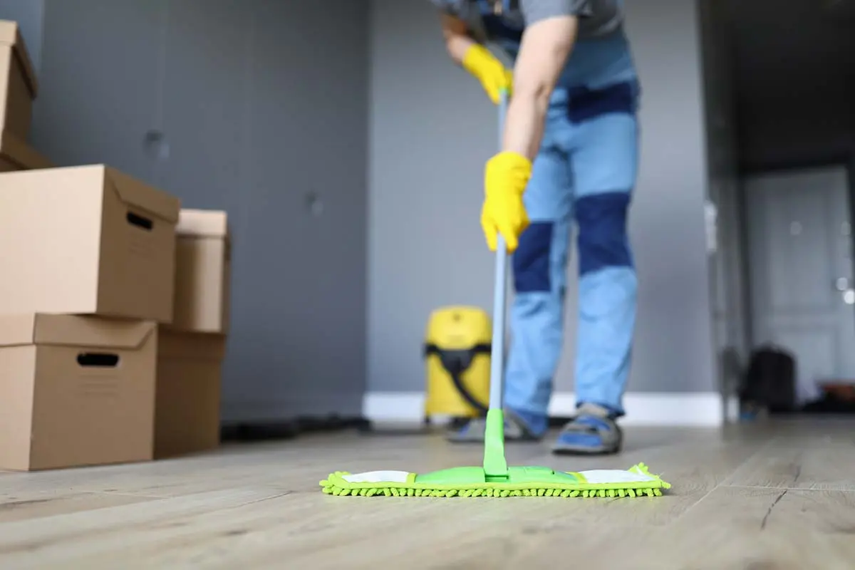 Cleaner in gloves mopping a hardwood floor with boxes stacked nearby.