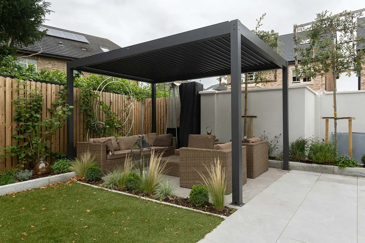 Outdoor seating area under a sleek pergola with wicker sofas, surrounded by greenery and decorative grasses.