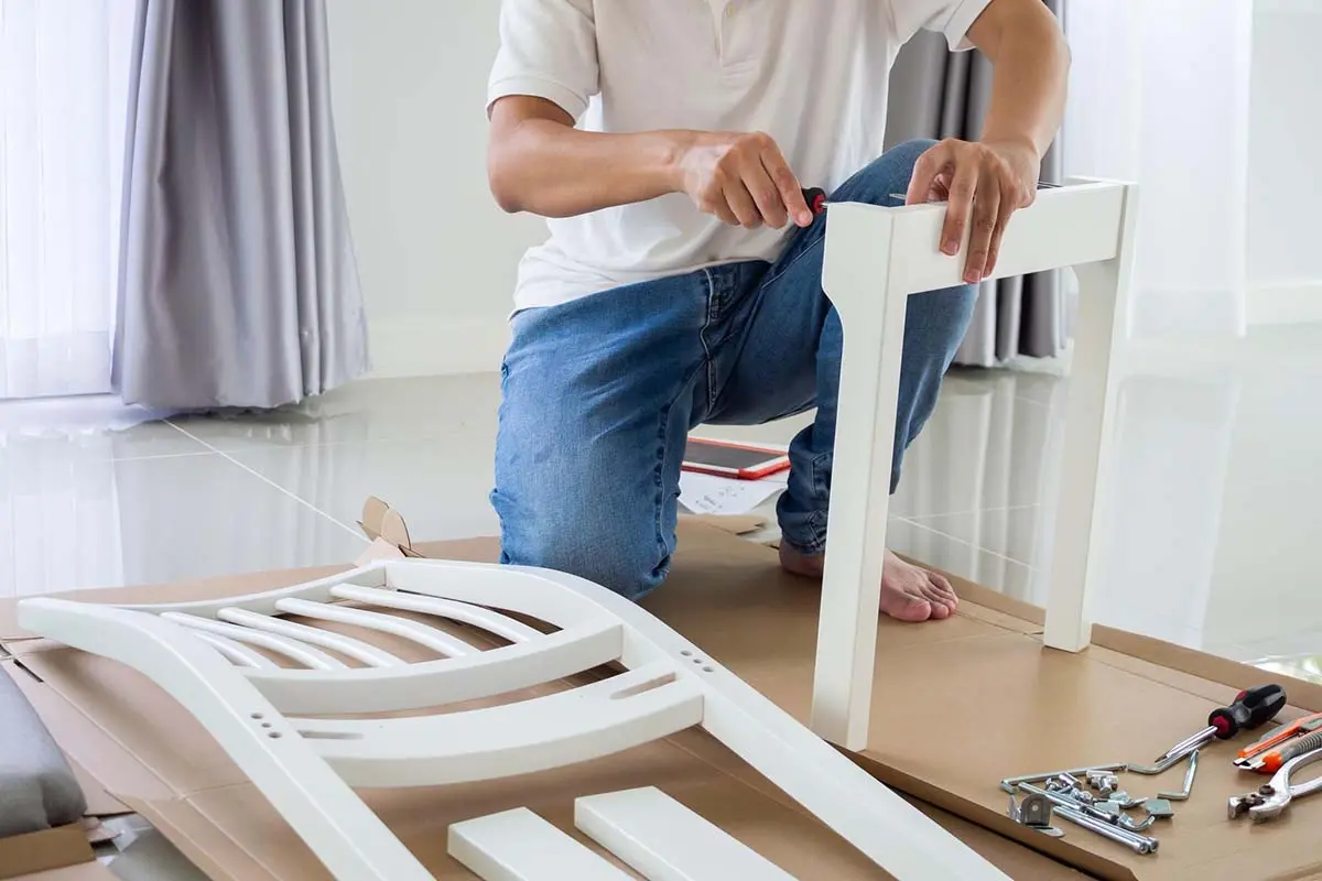Person assembling a white chair with a screwdriver.