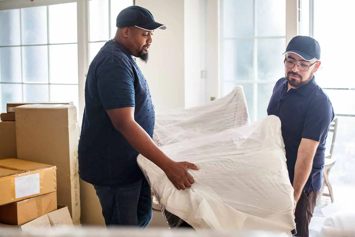 Two movers carefully lifting a wrapped piece of furniture.