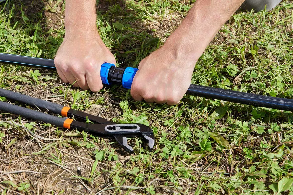 Installing or repairing a garden irrigation pipe with tools nearby.