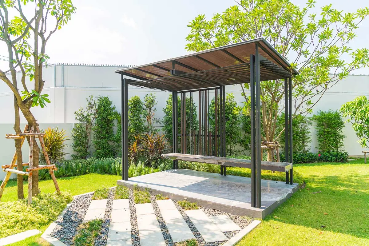 Modern garden pavilion with a sleek black frame, surrounded by lush greenery and a stone pathway.