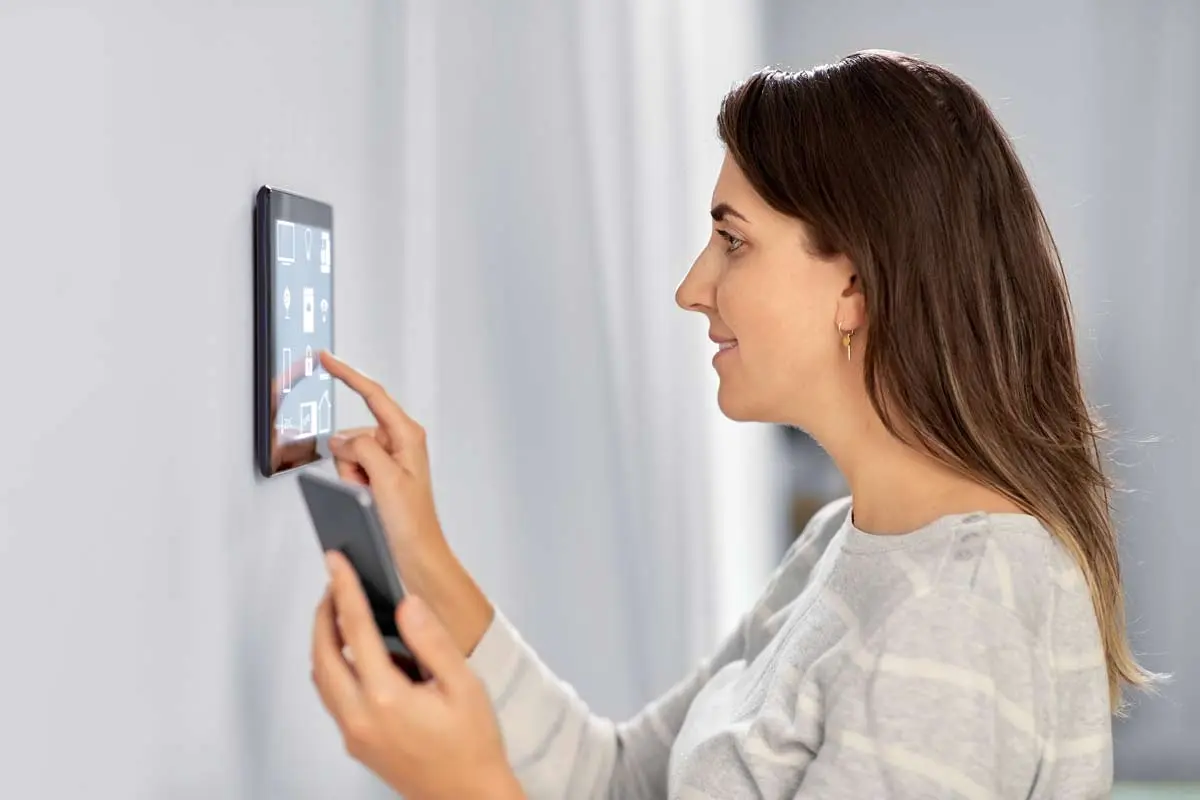 A woman interacting with a smart home control panel while holding a smartphone, showcasing seamless smart home integration.