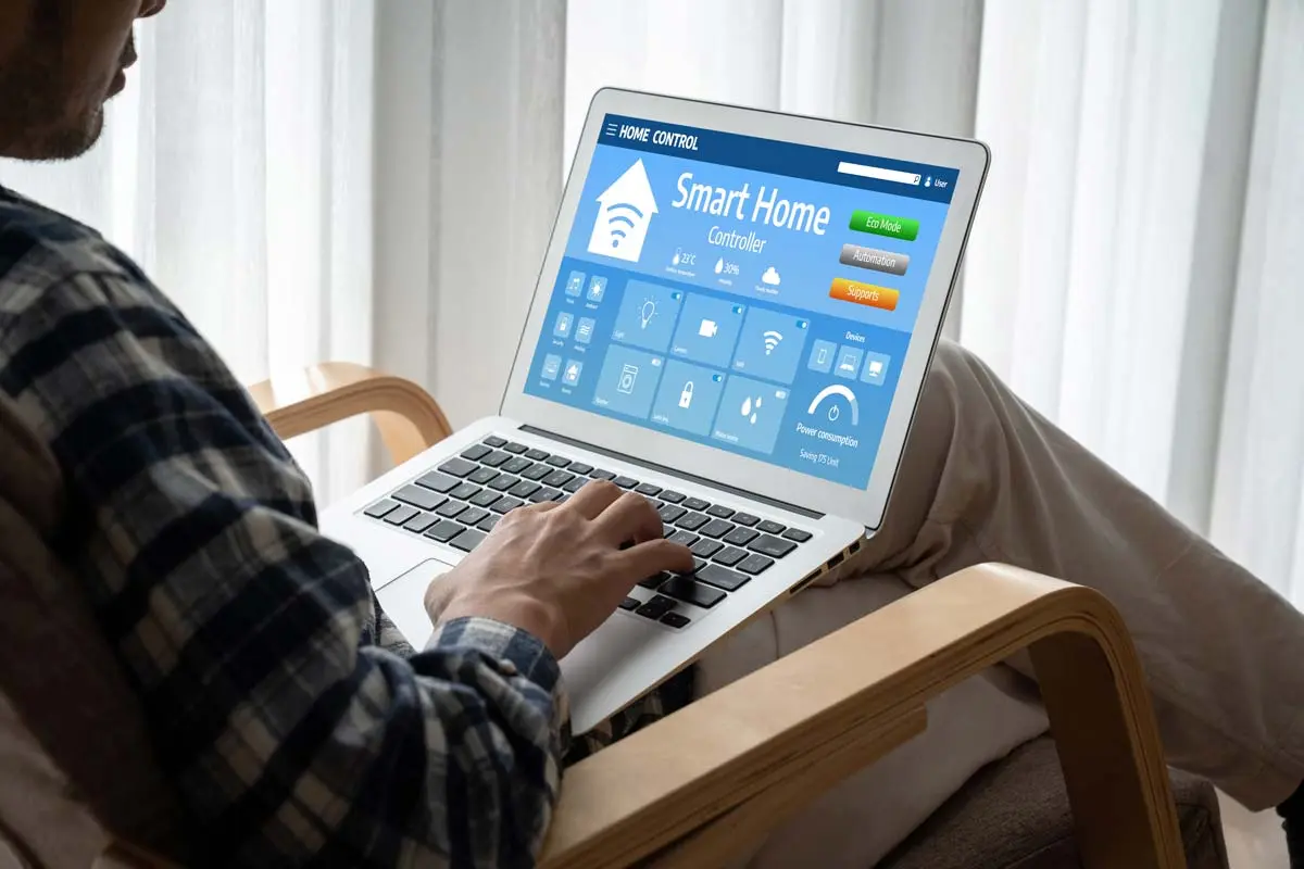 Man sitting on a chair using a laptop to control smart home devices and monitor energy usage.