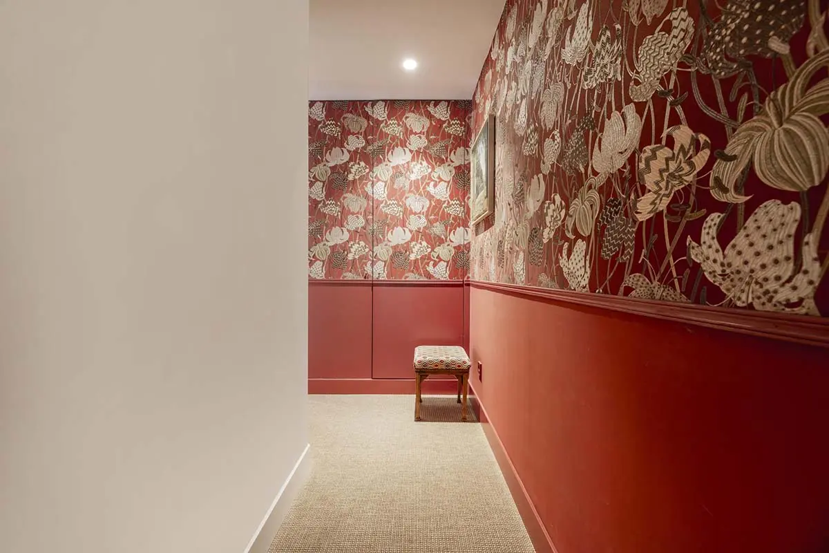 Hallway with floral red wallpaper, accent lighting, and a decorative bench.
