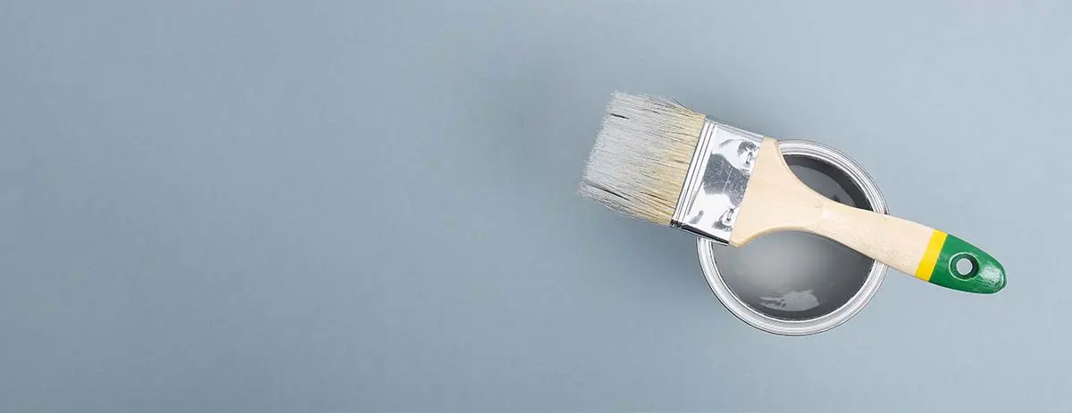 Paintbrush resting on a can of gray paint against a plain background.