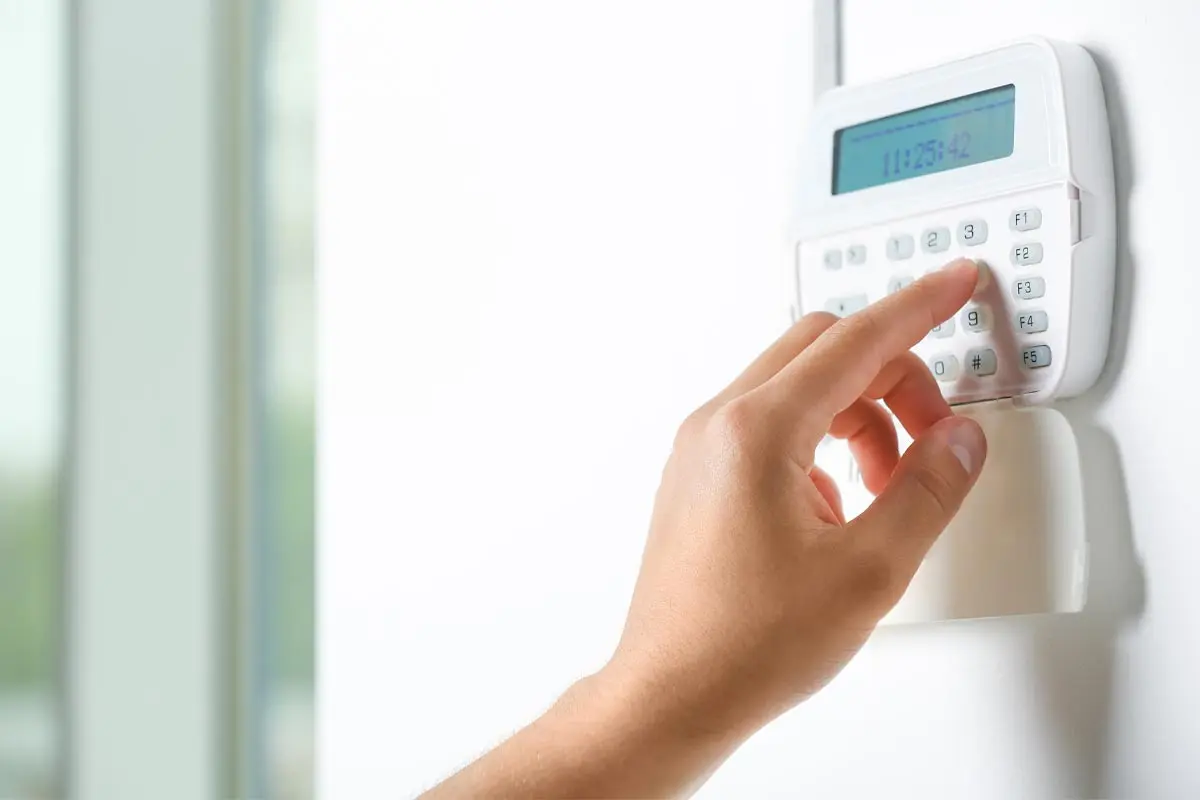 Hand entering a code on a wall-mounted home alarm keypad.