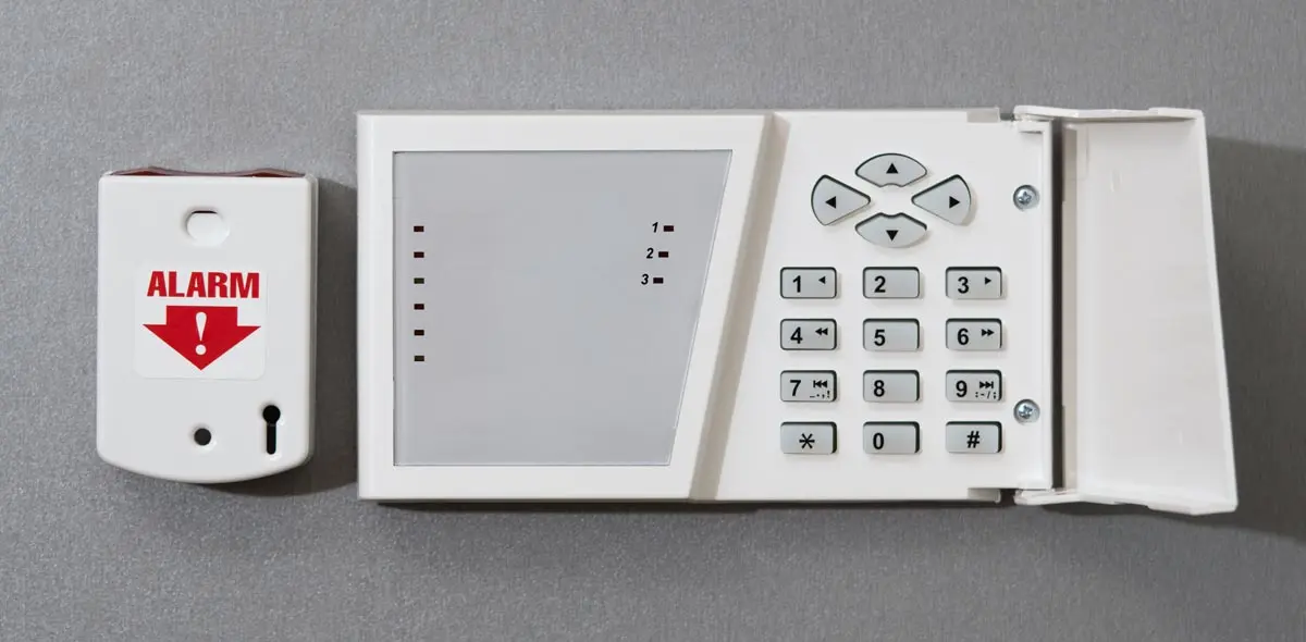 Security panel with alarm button and keypad on a gray wall.
