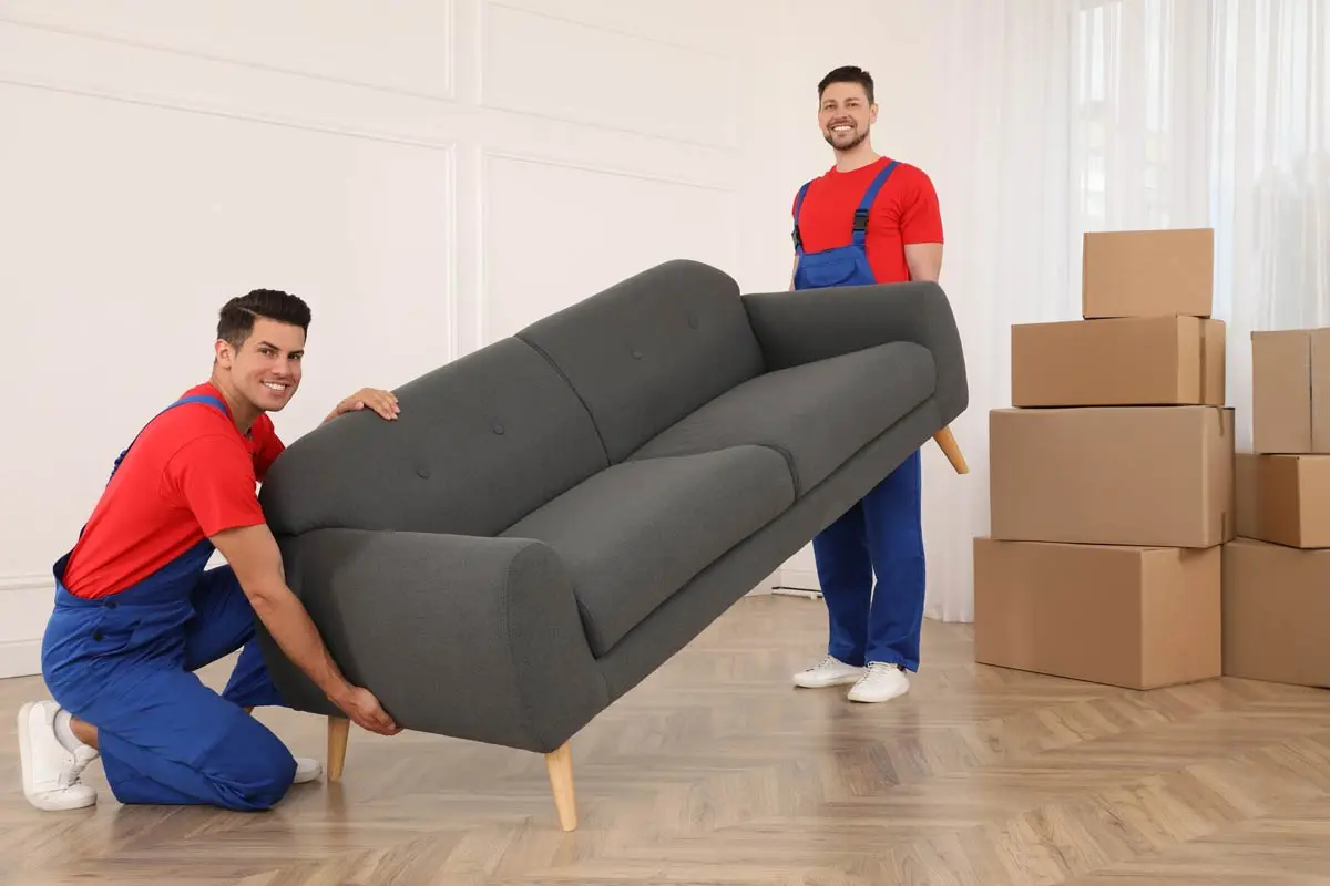 Two professional movers lifting a sofa beside stacked boxes.