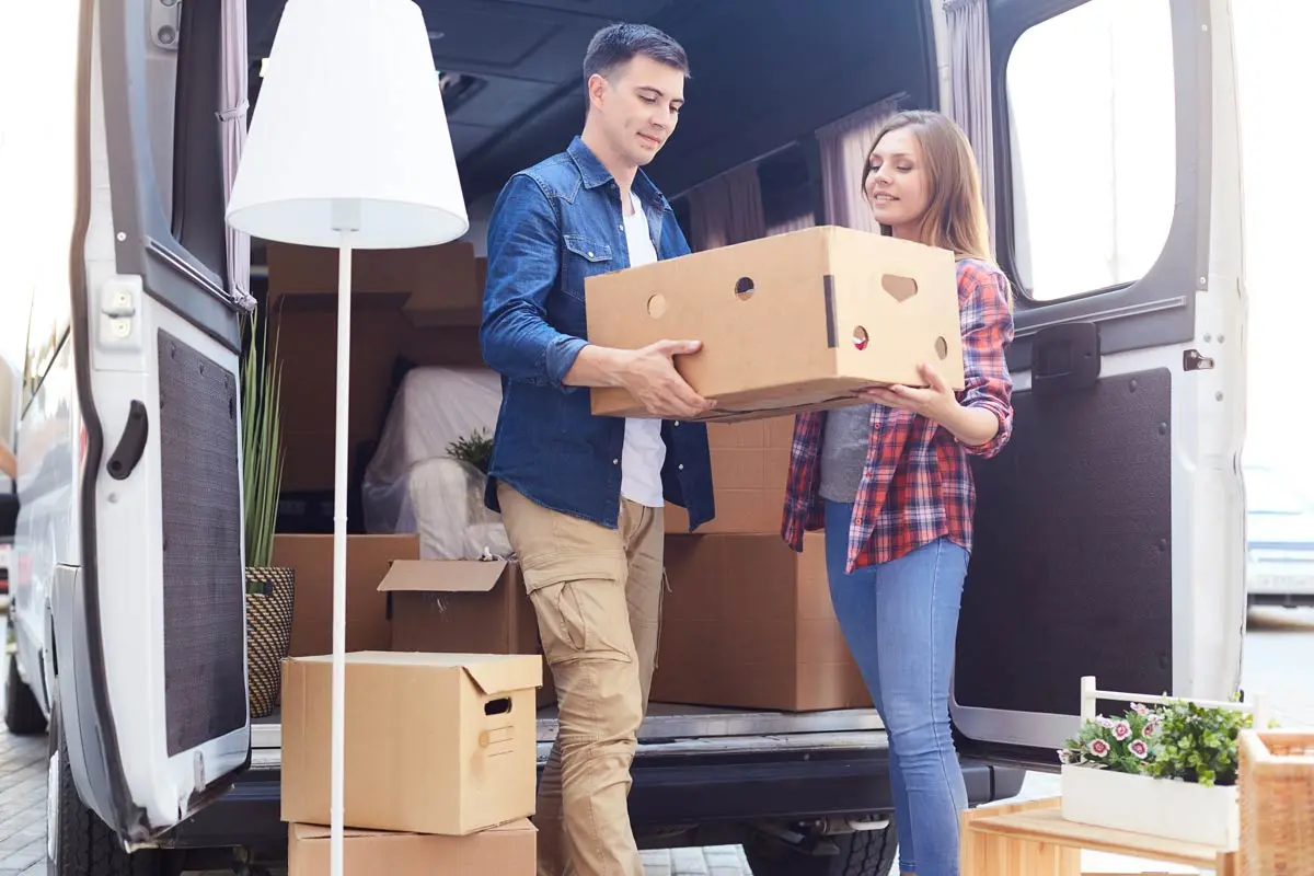 Couple unloading boxes from a small moving van.