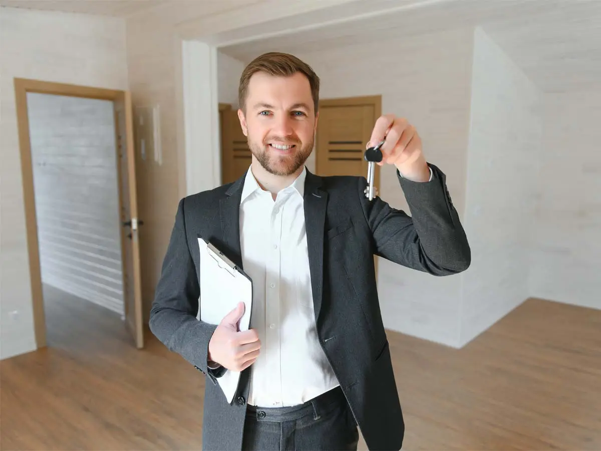 Smiling rental agent holding keys inside an empty, modern apartment.